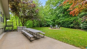 A picnic table with benches in a backyard with a house and dense trees. - Private pet-friendly escape w/ Views, Fenced Yard, Stocked kitchen, Fireplace (Maggie Valley)