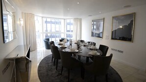 A modern dining room with a round table set for six, large windows, and a cityscape view. - Spacius 3-bed Apartment in Kensington, London (London)