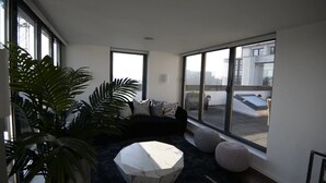 A modern living room with a black sofa, a white coffee table, and large windows offering a view of the cityscape. - Spacius 3-bed Apartment in Kensington, London (London)