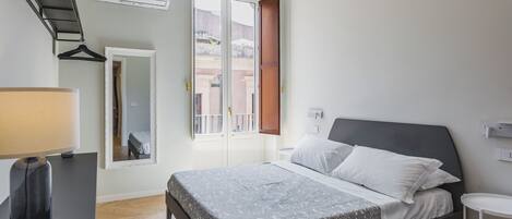 A bedroom with a bed, bedside table, lamp, mirror, and an air conditioning unit.