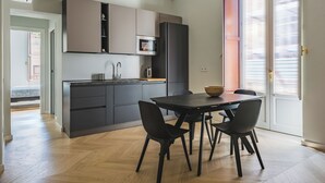A modern kitchen with grey cabinets, a black refrigerator, and a microwave. There is a dining table with four chairs and a bowl on it. - Palazzo Bozzanca by Wonderful Italy (Syracuse)