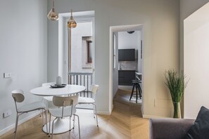 A modern dining area with a round table and chairs, a kitchen in the background, and a plant on the right. - Palazzo Bozzanca by Wonderful Italy (Syracuse)