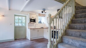 A modern kitchen with white cabinets, a microwave, and a sink. There is a wooden staircase with a white railing leading to another level. - The Stables - 2 Bedroom Cottage - Princes Gate (Narberth)