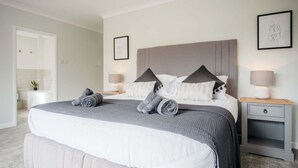 A modern bedroom with a large bed, two bedside tables, a nightstand, and a wall-mounted lamp. - Springfield Lodge - 3 Bedroom Home - Princes Gate (Narberth)