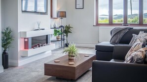 A modern living room with a fireplace, a sofa, a coffee table, and a large window with a view. - Springfield Lodge - 3 Bedroom Home - Princes Gate (Narberth)