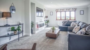 A modern living room with a sofa, coffee table, and a fireplace. There are plants and a mirror on the shelves. - Springfield Lodge - 3 Bedroom Home - Princes Gate (Narberth)