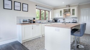 A modern kitchen with white cabinetry, a central island, and a bar stool. - Springfield Lodge - 3 Bedroom Home - Princes Gate (Narberth)