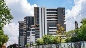 Un immeuble moderne à plusieurs étages, dont la façade est un mélange de verre et de béton, situé près d’une route où est affiché un panneau indiquant la limite de vitesse.