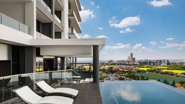 Un hôtel moderne doté d’une piscine à débordement sur le toit, offrant une vue sur les toits de la ville et donnant sur un jardin aménagé.