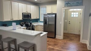 A kitchen with white cabinets, a stainless steel refrigerator, a microwave, and a bar stool area. - Luxury 3 Bedroom Villa @ N. Beach Resort - Walk to Everything! Beach/Pools/Food (North Myrtle Beach)