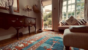 A room with a patterned rug, a sofa with striped cushions, a wooden cabinet, and a large window with curtains. - Scallop Cottage Oasis of Calm - Pass the Keys (Rye)
