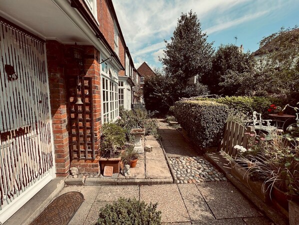 Stroll through the serene garden, lined with lush greenery and a brick wall, featuring a charming outdoor seating area.