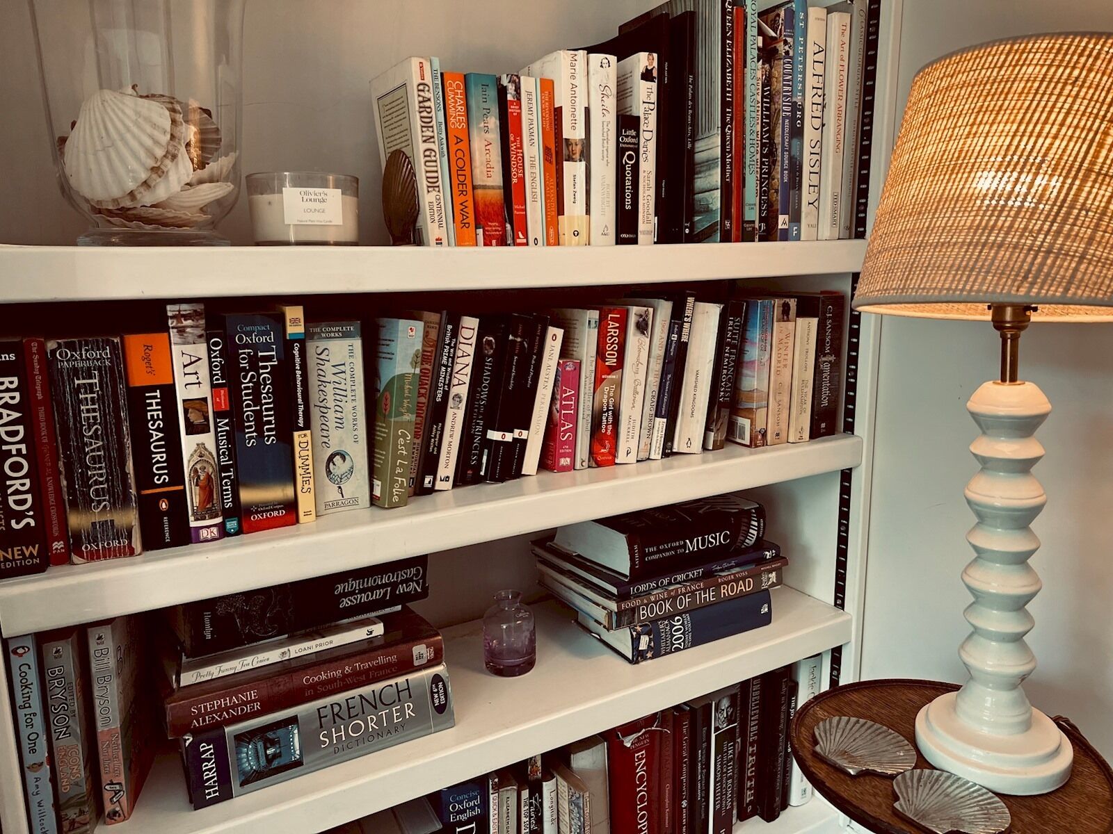 A bookshelf filled with books, a decorative shell, a candle, and a lamp.