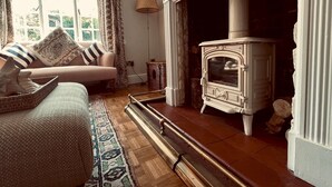 A cozy living room with a fireplace, a sofa with patterned cushions, a floor lamp, and a woven basket on the floor. - Scallop Cottage Oasis of Calm - Pass the Keys (Rye)