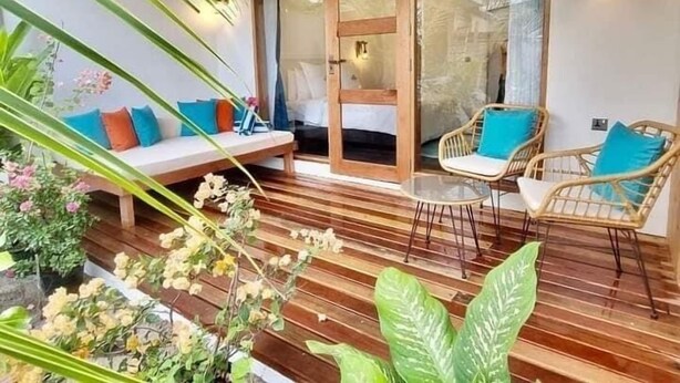 Un área de estar al aire libre acogedora con una terraza de madera, sillas de mimbre y un banco acolchado con cojines de colores.