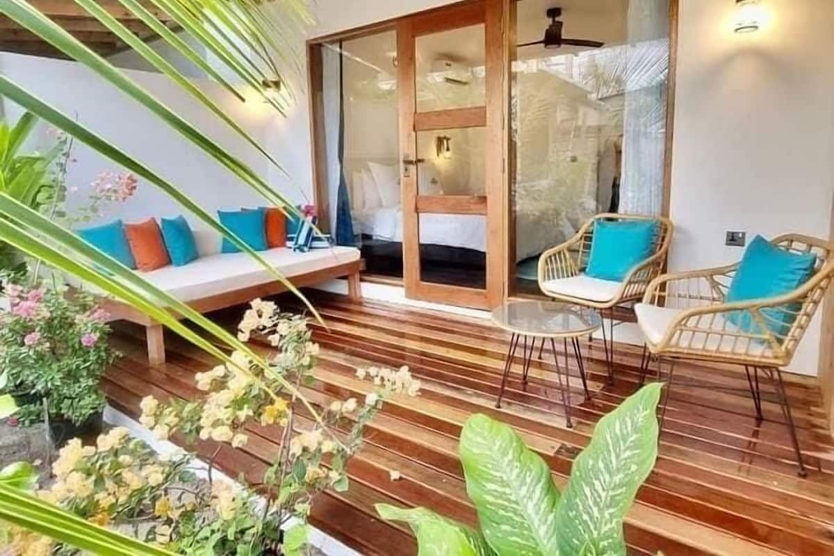 A cozy outdoor seating area with a wooden deck, wicker chairs, and a cushioned bench with colorful cushions.