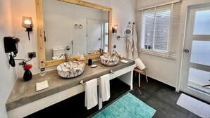 Un baño moderno con un espejo grande, dos lavamanos, un perchero para toallas y una ventana con persianas.