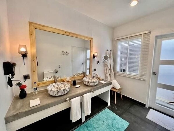 A modern bathroom with a large mirror, two sinks, a towel rack, and a window with blinds. - Seaside Dhigurah (Dhigurah)