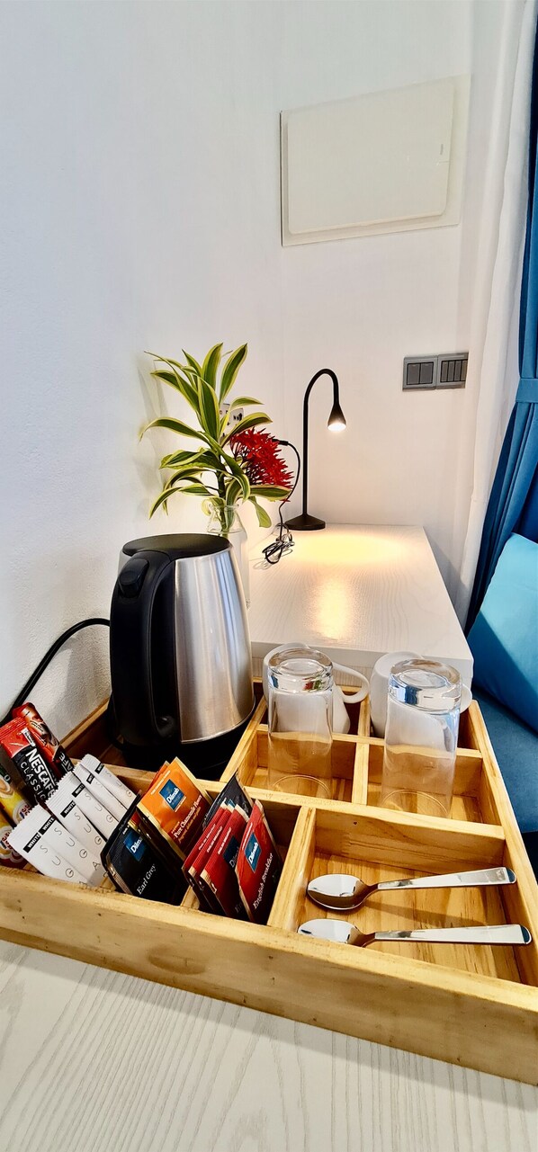 Una kitchenette ordenada con tetera, cafetera y una bandeja con condimentos y utensilios.