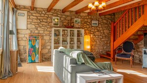 A cozy living room with a stone wall, wooden beams, a staircase, and a comfortable sofa.
