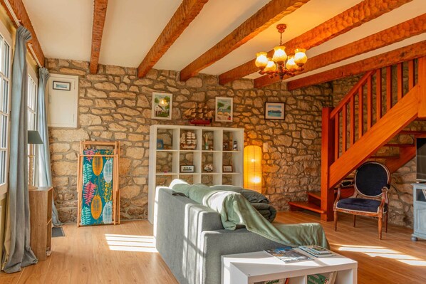 Un salon chaleureux avec un mur en pierre, des poutres en bois, un escalier et un canapé confortable.