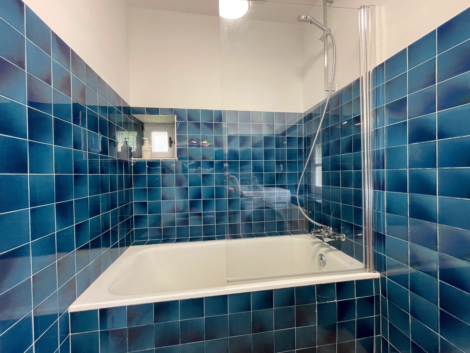 Une salle de bain avec des murs recouverts de carreaux bleus, une baignoire blanche et un espace douche délimité par des parois en verre.
