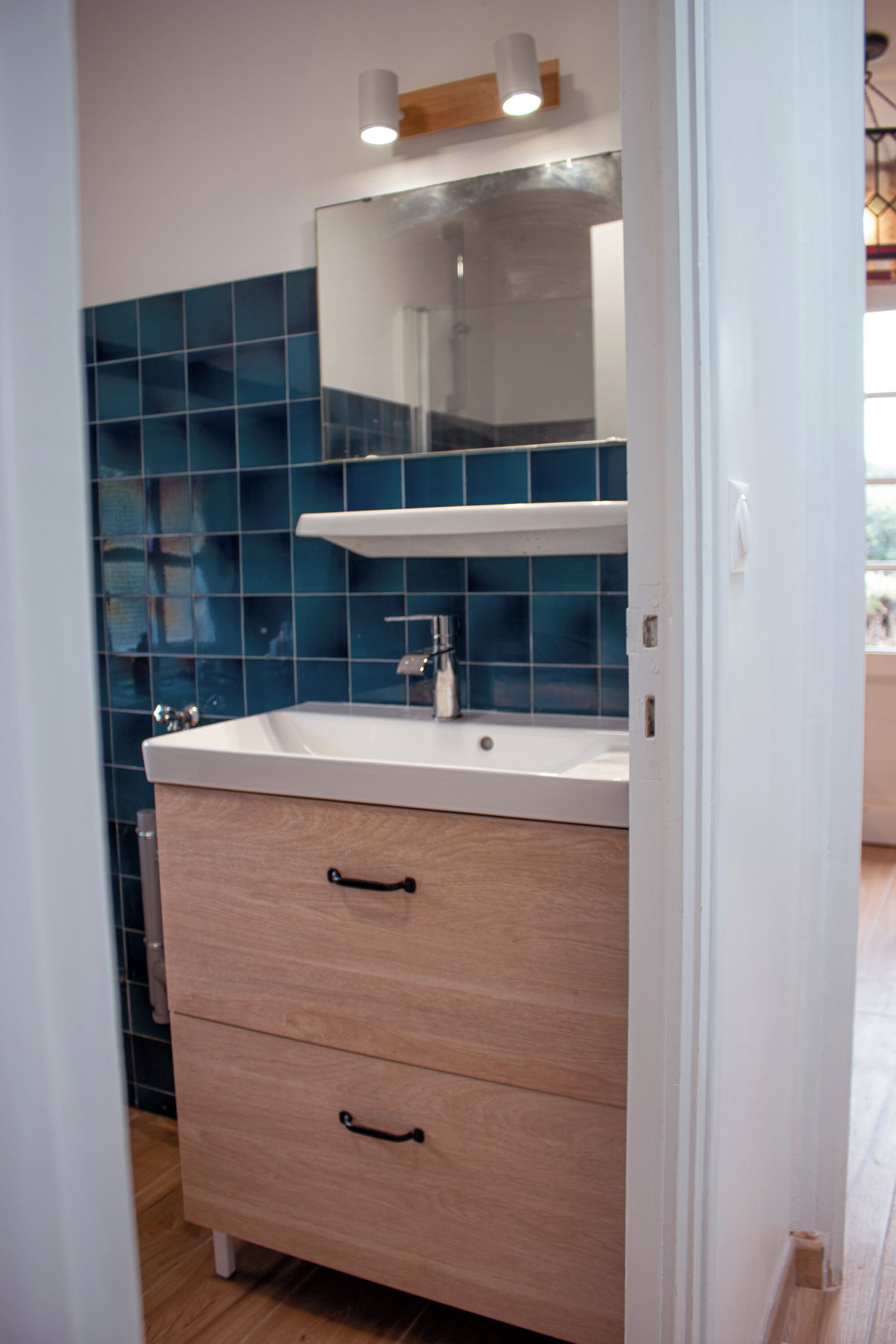 A bathroom with a white sink, wooden cabinet, and blue tiles.