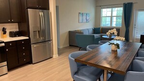 A modern kitchen with dark cabinets, stainless steel appliances, and a wooden dining table with blue chairs. - Modern 3B2b APT near Convention Center Universal 7 (Orlando)
