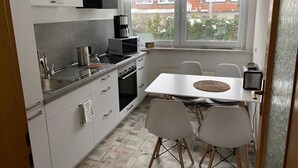 Eine kompakte Küche mit weißen Schränken, einem Herd und einem Essbereich mit Tisch und Stühlen.