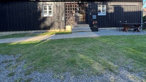 Ein zweigeschossiges Holzhaus mit rotem Ziegeldach, Holzzaun und einem Schotterweg.