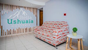 A hotel lobby with a sofa covered in a red and white pattern, a small table with a plant, and a wall with a logo and text. - Hostería Bella Ushuaia (Ushuaia)
