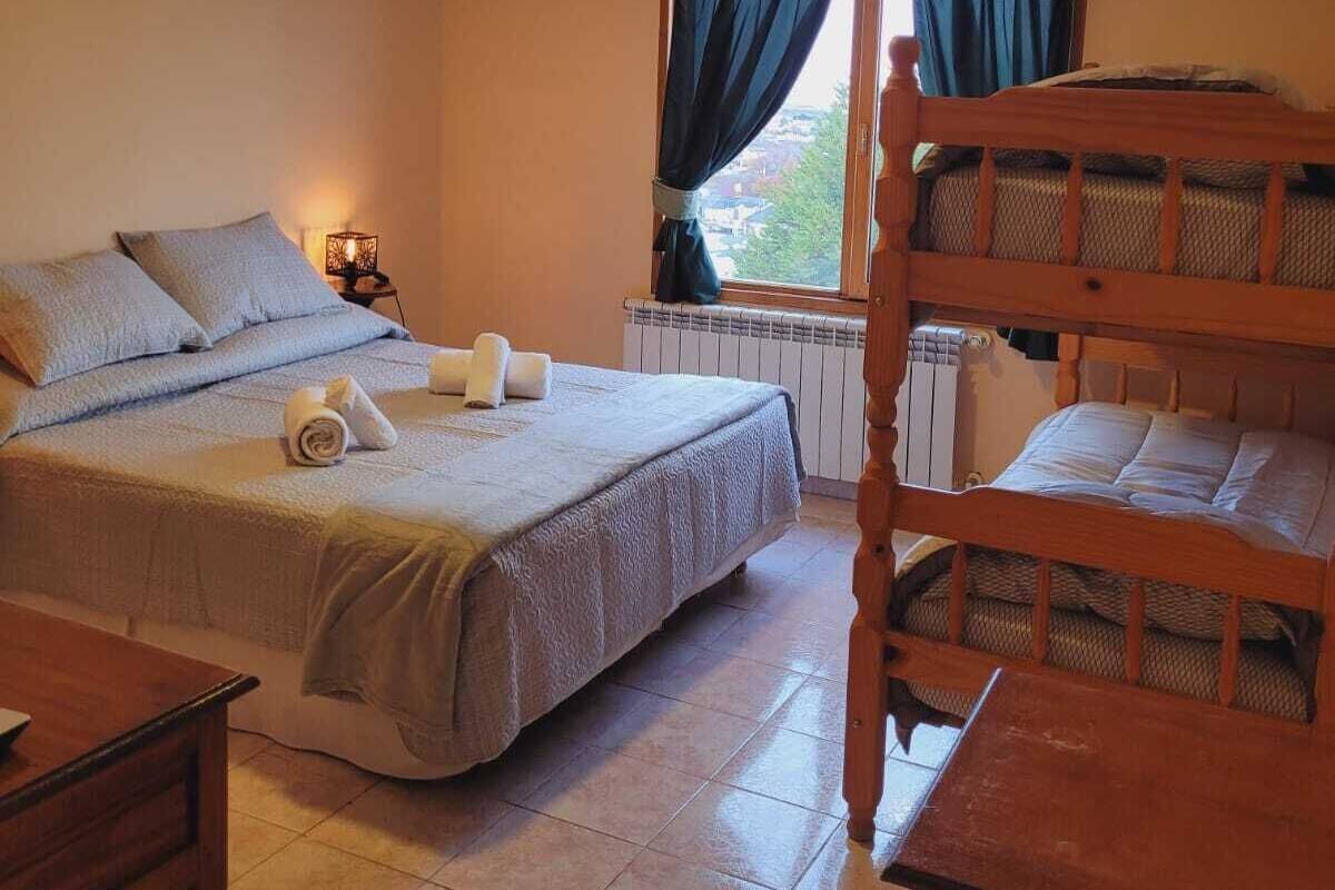 A bedroom with a single bed, a bunk bed, a bedside table, a lamp, and a window with curtains.