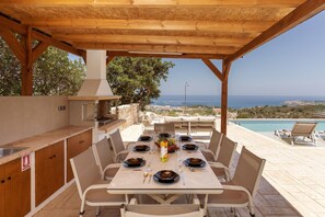 Enjoy al fresco dining with a grill and sink nearby, overlooking the pool and scenic coastline views.