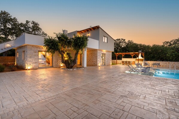 Relax by the pool surrounded by a spacious outdoor area with a pergola providing shade.