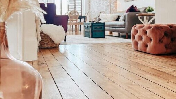 Amplia sala de estar con piso de madera, un sofá mullido, un reposapiés tapizado y un jarrón grande con plumas de pájaro.