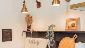 Una cocina con un lavabo blanco, armarios de madera, una estufa y dos lámparas colgantes de latón.