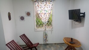 A room with two wooden chairs, a small wooden table with a remote, a TV mounted on the wall, and a window with a floral curtain. - Cabaña Encanto del Viento, casa frente al mar.
Se admiten mascotas  (San Bernardo del Viento)