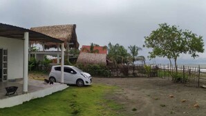 A white car parked in a driveway with a thatched-roof house and a fenced area with palm trees. - Cabaña Encanto del Viento, casa frente al mar.
Se admiten mascotas  (San Bernardo del Viento)