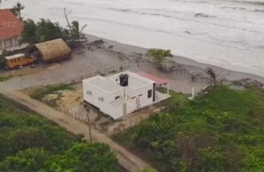 Un bâtiment situé sur la côte, avec un toit rouge, jouxtant une plage et une construction dont le toit est fait de chaume.
