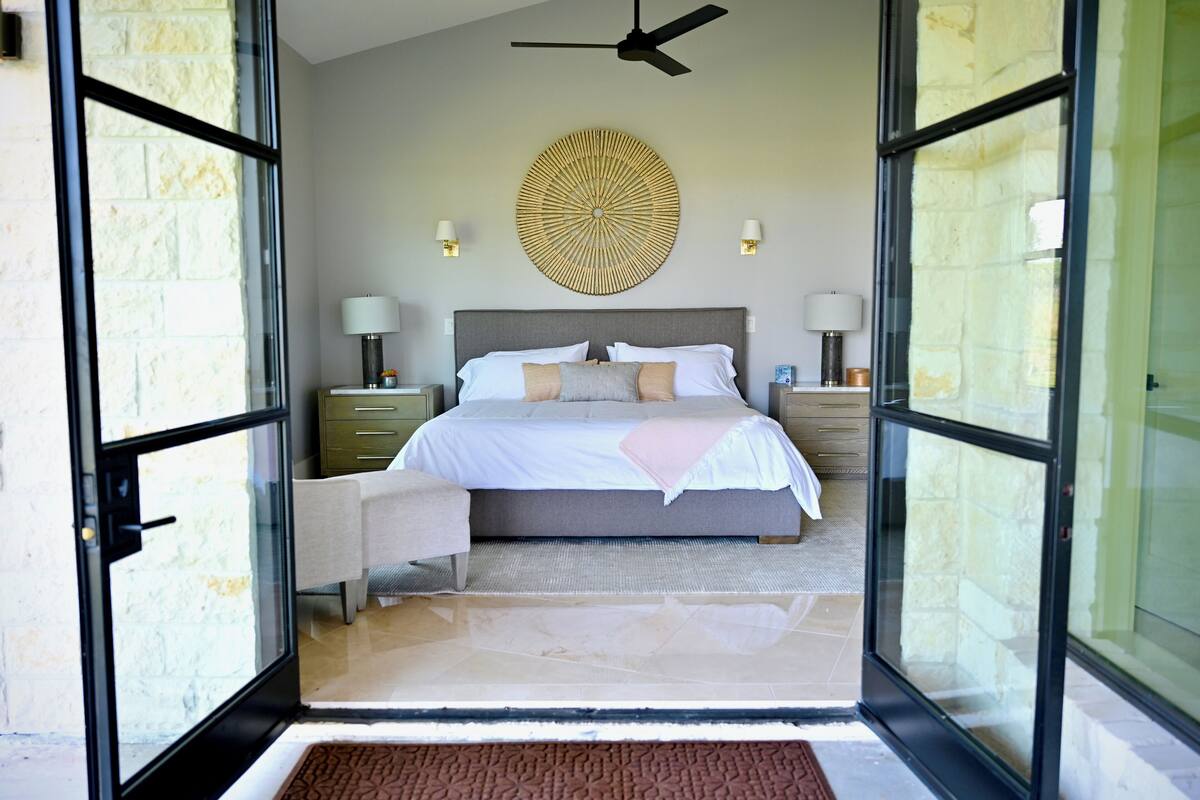 A bedroom with a bed, bedside tables, lamps, a decorative wall piece, and a ceiling fan.