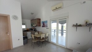 A compact living space with a kitchenette, a dining area with chairs, a sofa, and a sliding glass door leading to an outdoor area. - Apartment With a Pool, Mountainview, Near the Sea! (Posedarje)