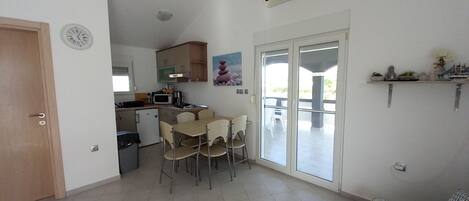 A compact living space with a kitchenette, a dining area with chairs, a sofa, and a sliding glass door leading to an outdoor area.