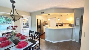 A modern kitchen with a central island, a dining area with red tableware, and a view of the outdoors. - Townhouse by the River (Birmingham)
