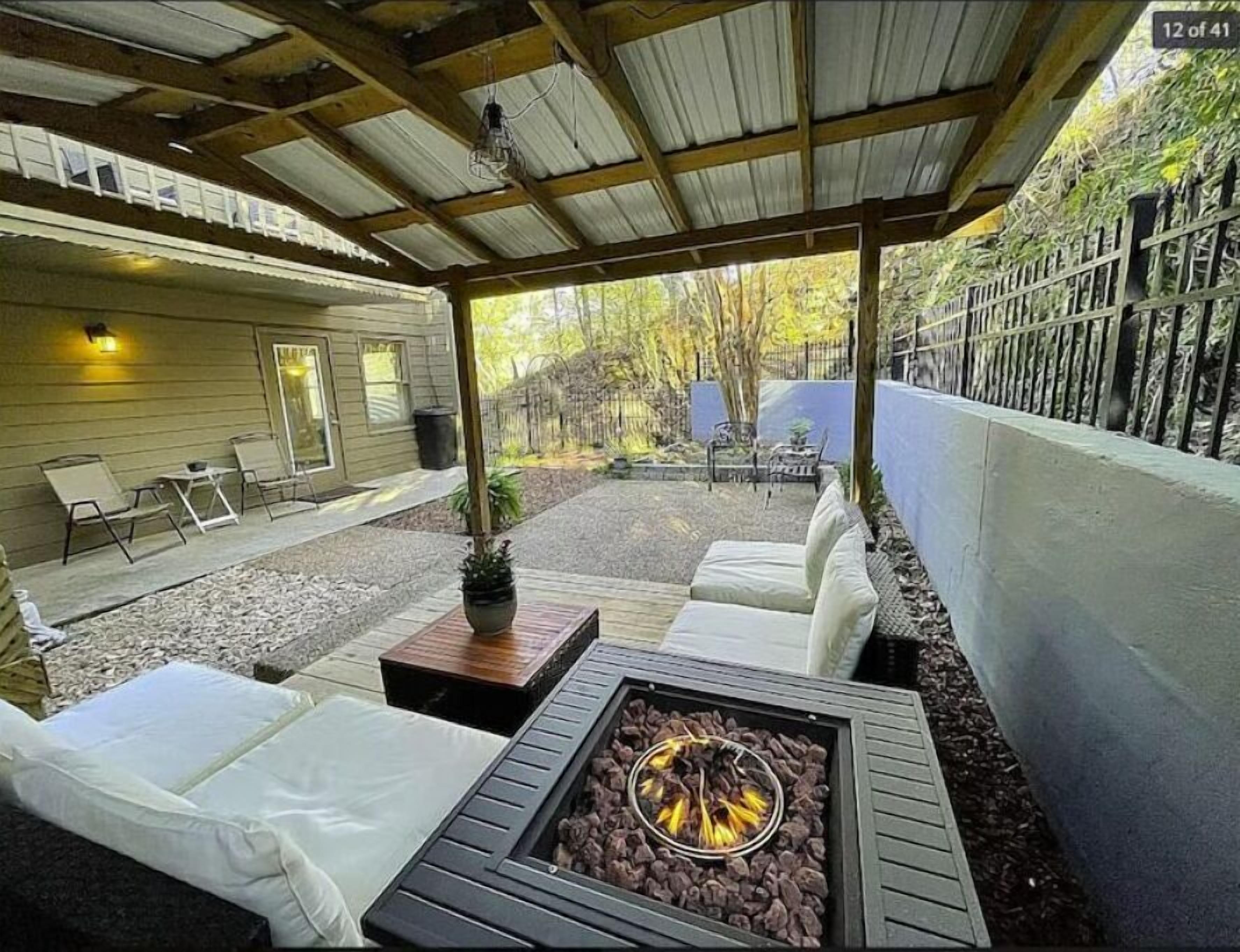 A covered patio area with a fire pit, outdoor seating, and a view of a house.