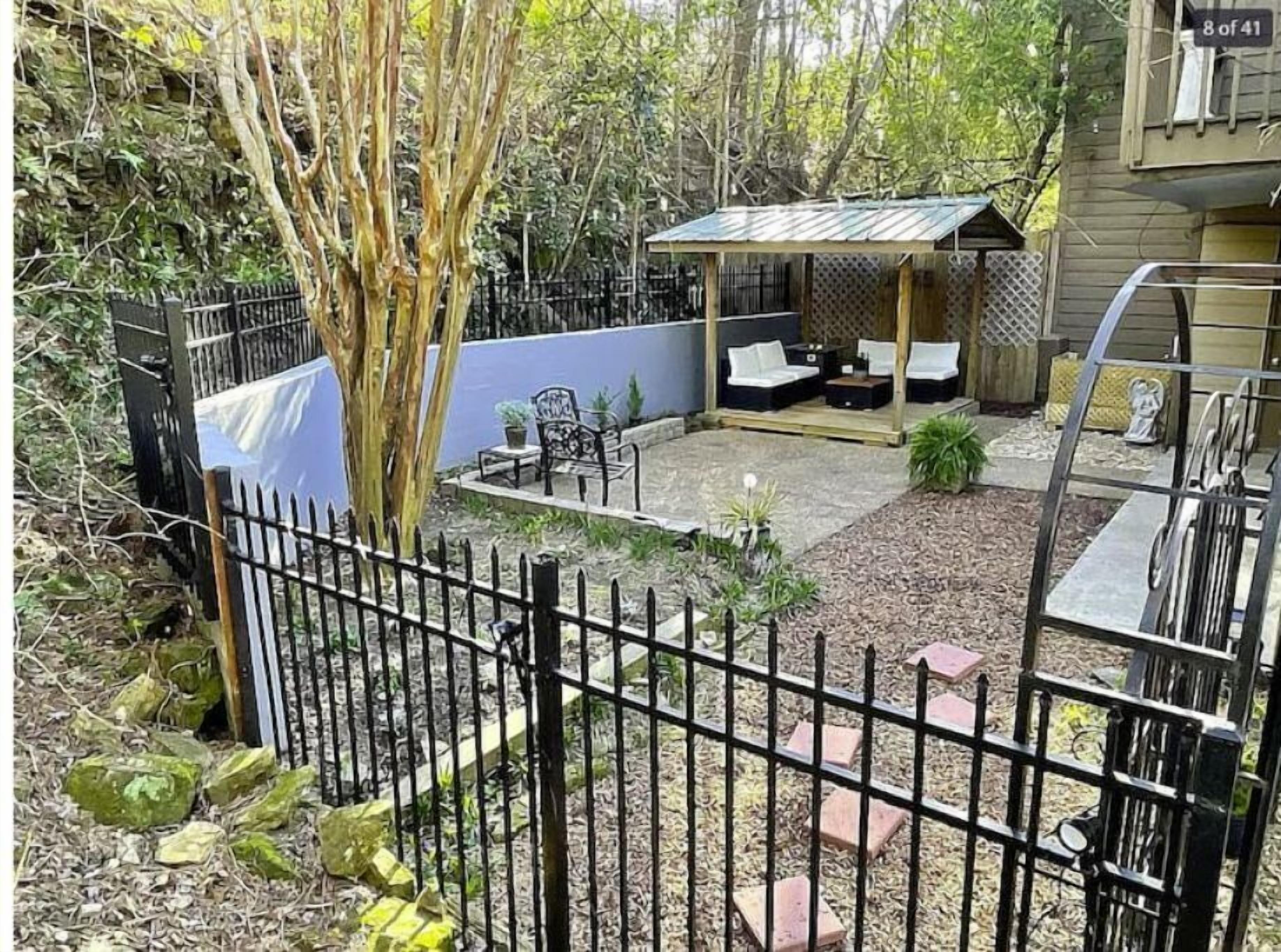 Un patio trasero cercado con zona de patio, mobiliario exterior y una pequeña estructura cubierta.