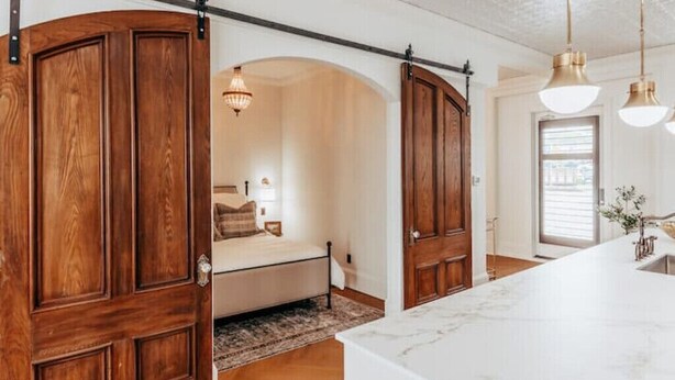Una habitación con una puerta grande de madera, una cama con cabecera blanca, una araña y una encimera de mármol.