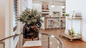Una cocina moderna con una mesa de vidrio, un jarrón decorativo con plantas y un carrito metálico con utensilios de cocina.