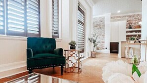 Un salón amplio con un sillón verde, una mesa de centro de mármol y un arreglo floral blanco.