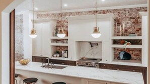Una cocina con armarios blancos, encimera de mármol y lámparas colgantes.