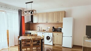 Uma cozinha compacta com armários de madeira, máquina de lavar, geladeira e um espaço de jantar com mesa e cadeiras.